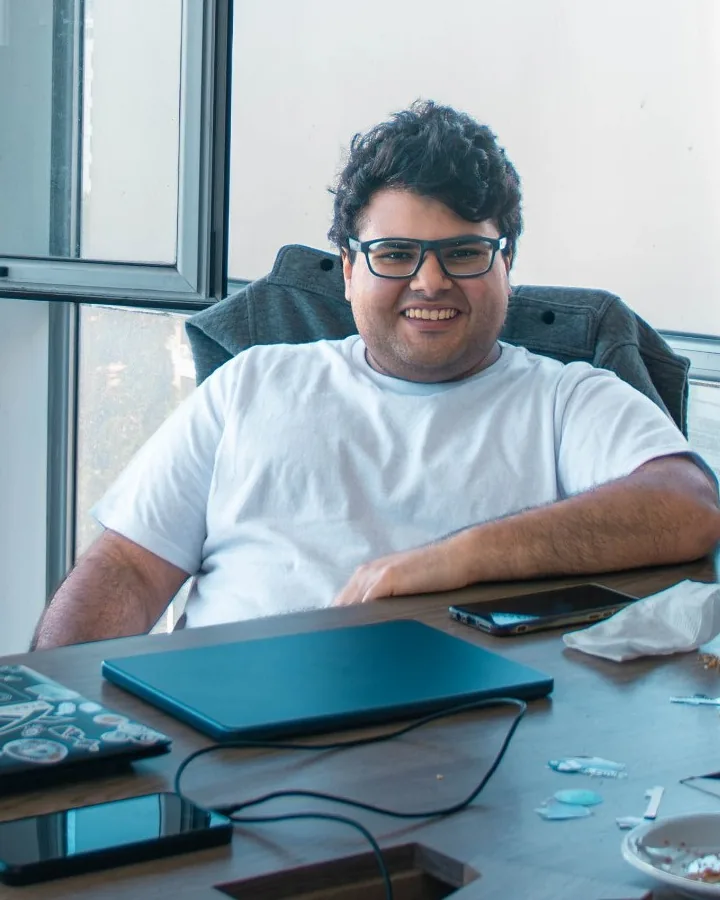 Francisco Perez sonriendo en una oficina, sentado frente a una mesa con laptops